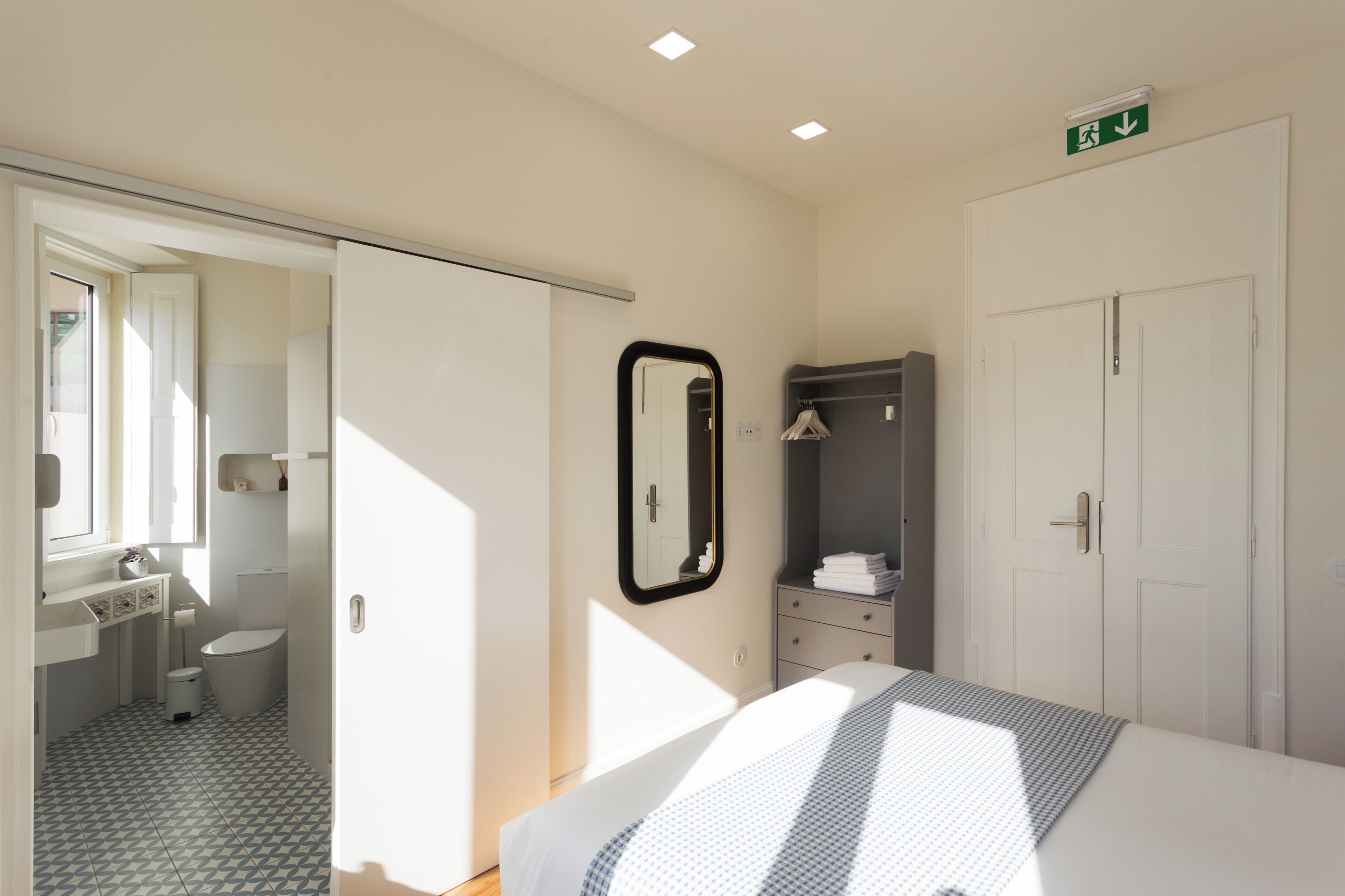 A hotel room with a bed, a wardrobe, a mirror, a sink, and a toilet.