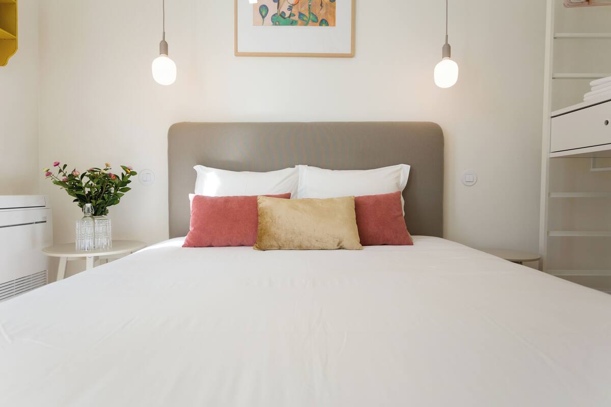 A neatly made bed with a headboard, two bedside lamps, and a small table with a vase of flowers.