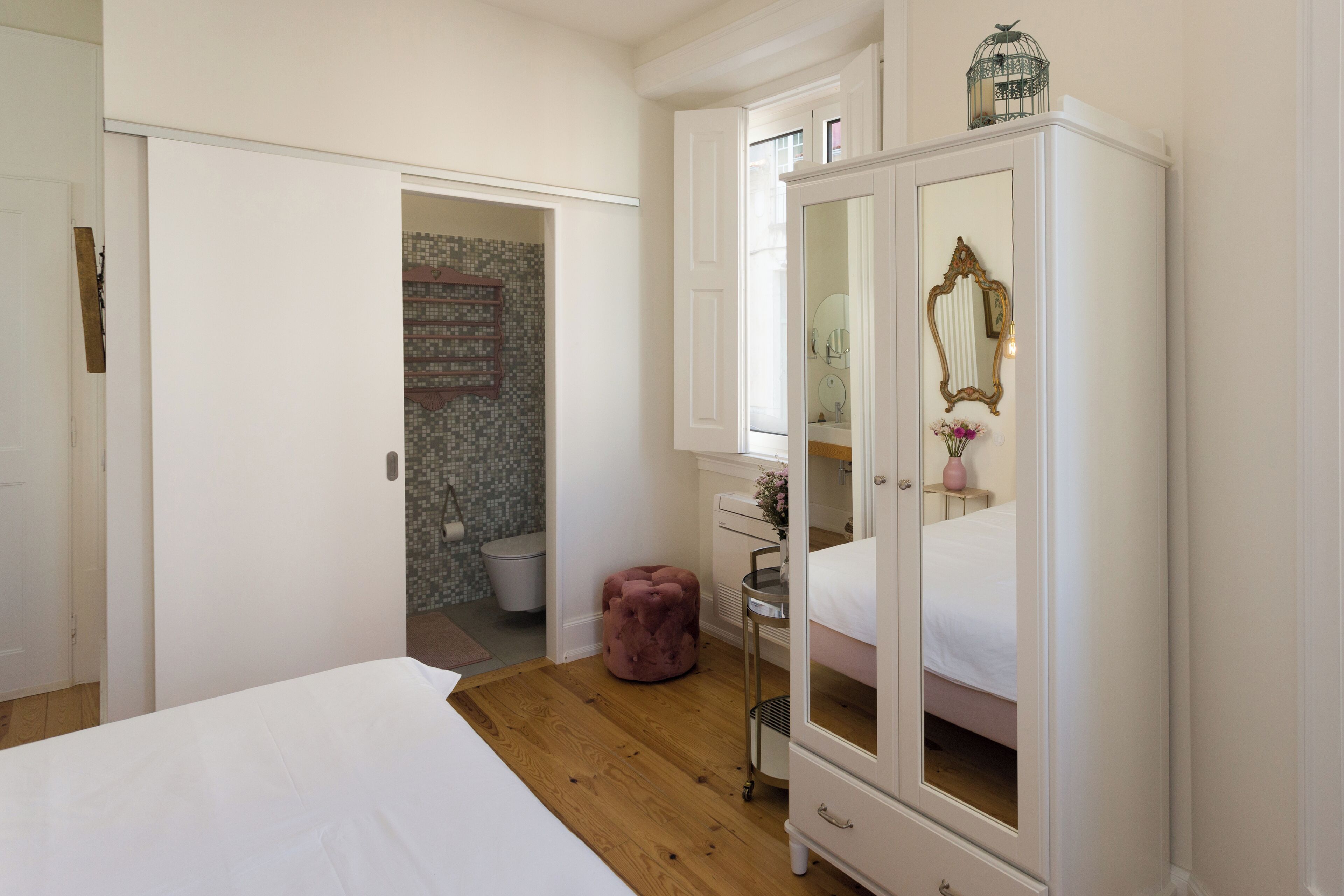 A bedroom with a bed, a wardrobe, a vanity with a mirror, and a small stool.