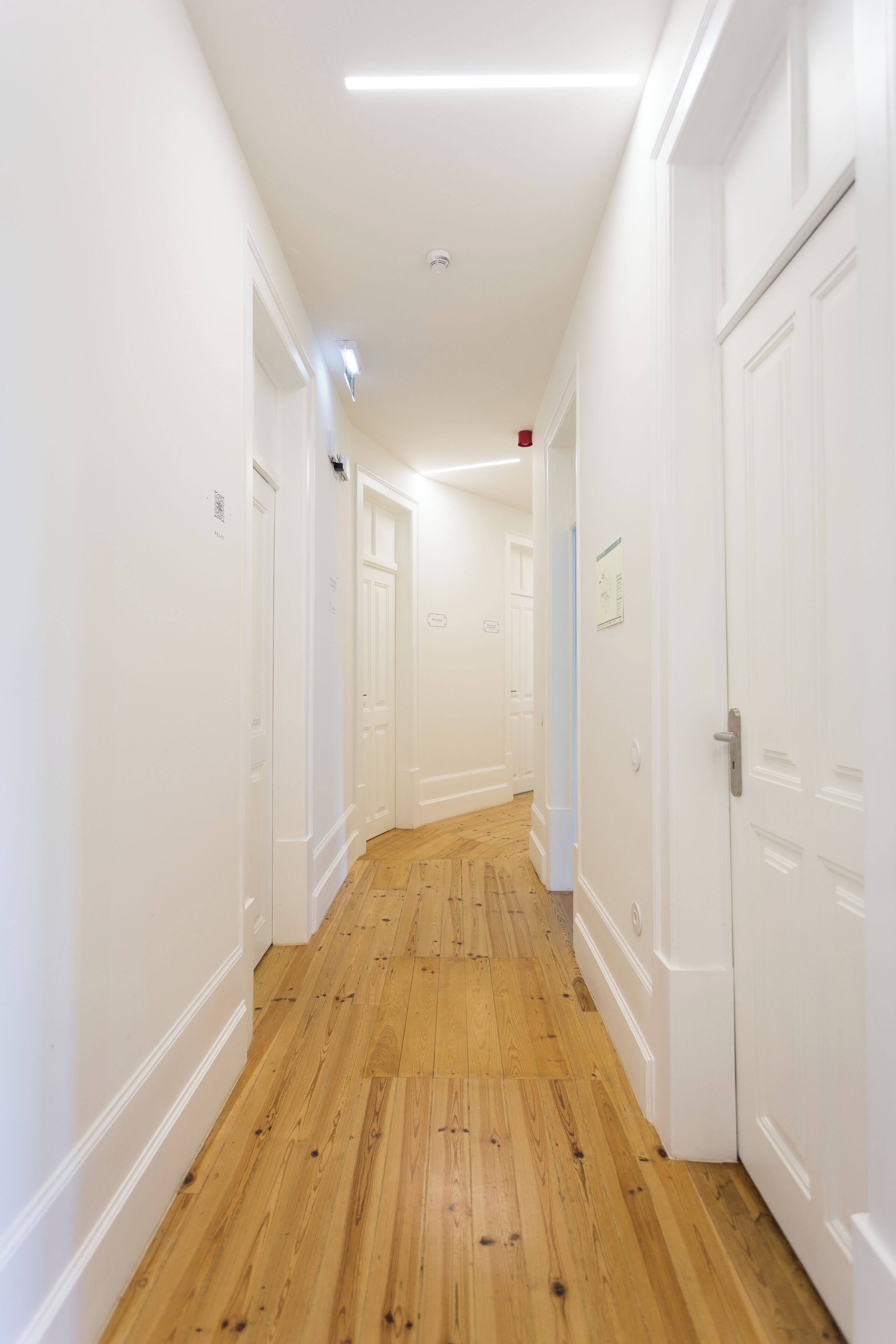 A narrow hallway with wooden flooring and white walls, leading to multiple doors.