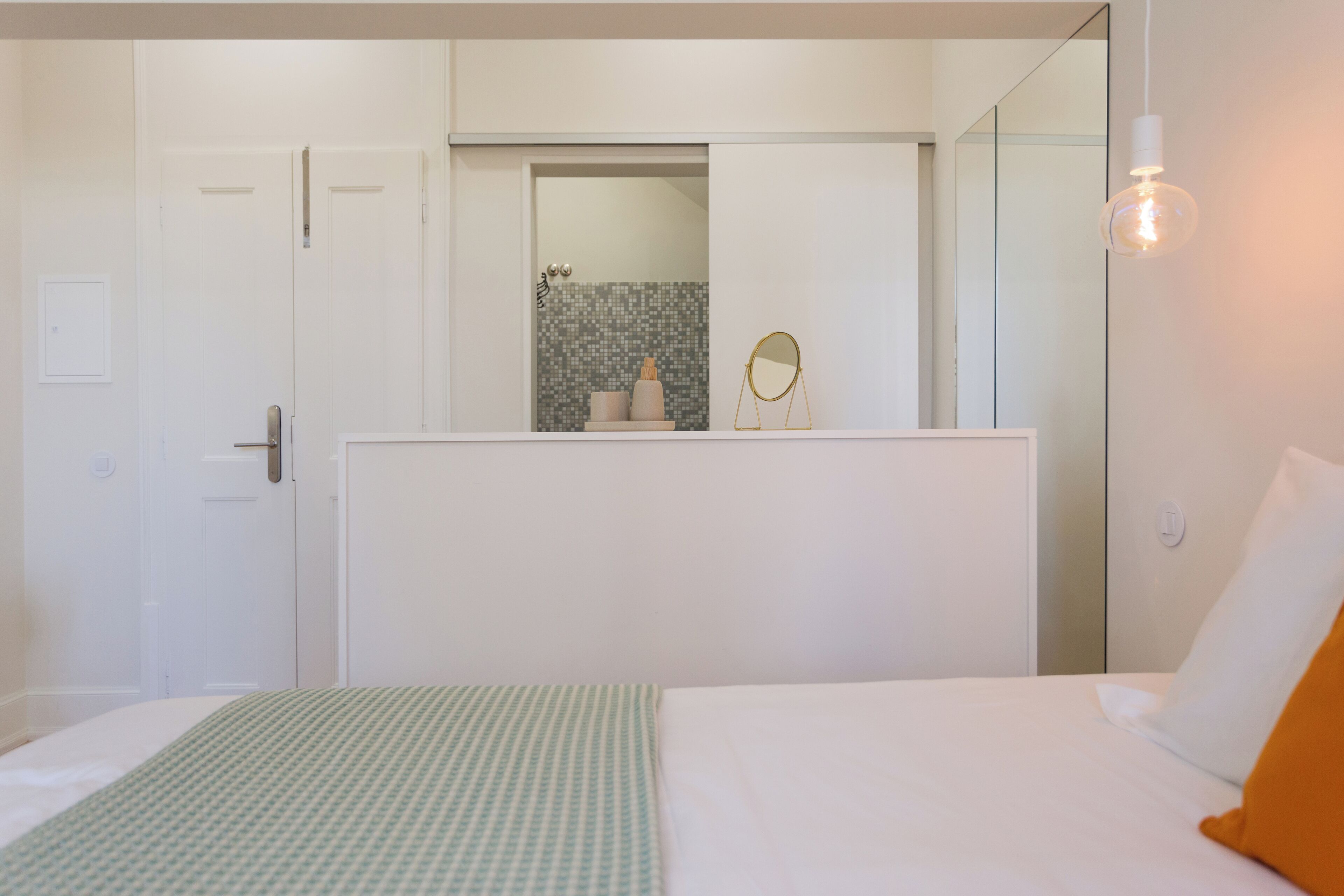 Une chambre d’hôtel avec un lit, une commode, un miroir et une salle de bain visible à travers une porte ouverte.