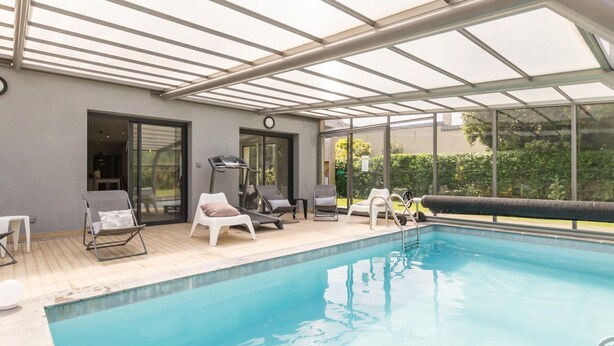 Una piscina interior con techo de cristal, sillas de descanso, una cinta de correr y un tobogán pequeño.
