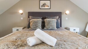 Un dormitorio con techo inclinado, una cama grande con almohadas mullidas, dos mesitas de noche y un cuadro enmarcado en la pared.
