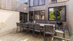 Un patio moderno al aire libre con terraza de madera, una mesa de comedor con sillas y una parrilla.