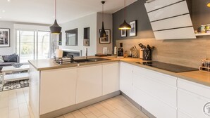 Una cocina moderna con armarios blancos, una isla central, iluminación colgante y vistas al área de estar.