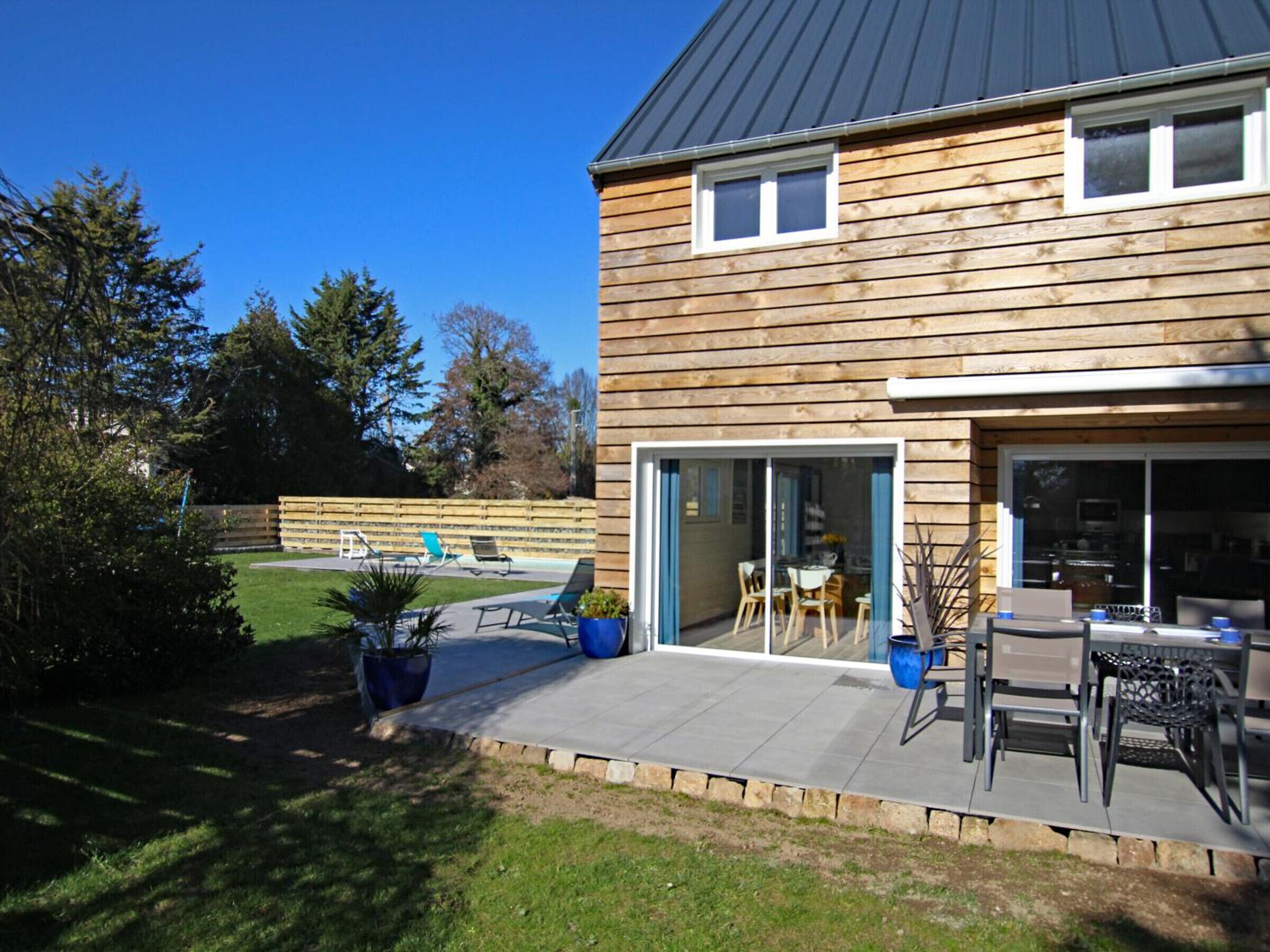 A modern house with a wooden exterior, a patio with outdoor furniture, and a visible kitchen area.
