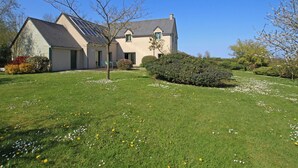 A two-story house with a sloped roof, a garage, and a small garden with flowers and shrubs. - Spacious house with garden near Utah Beach (Sainte-Marie-du-Mont)