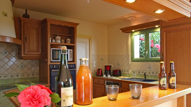 A kitchen with wooden cabinets, a microwave, a sink, and a window with flowers. - Spacious house with garden near Utah Beach (Sainte-Marie-du-Mont)