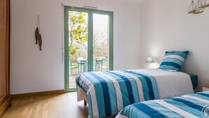 A bedroom with a bed, a nightstand, a lamp, and a view through a glass door to an outdoor area with chairs and a table. - Spacious house with garden near Utah Beach (Sainte-Marie-du-Mont)