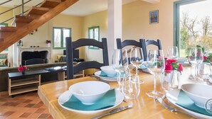 A dining area with a wooden table set for four, a fireplace, and a staircase. - Spacious house with garden near Utah Beach (Sainte-Marie-du-Mont)