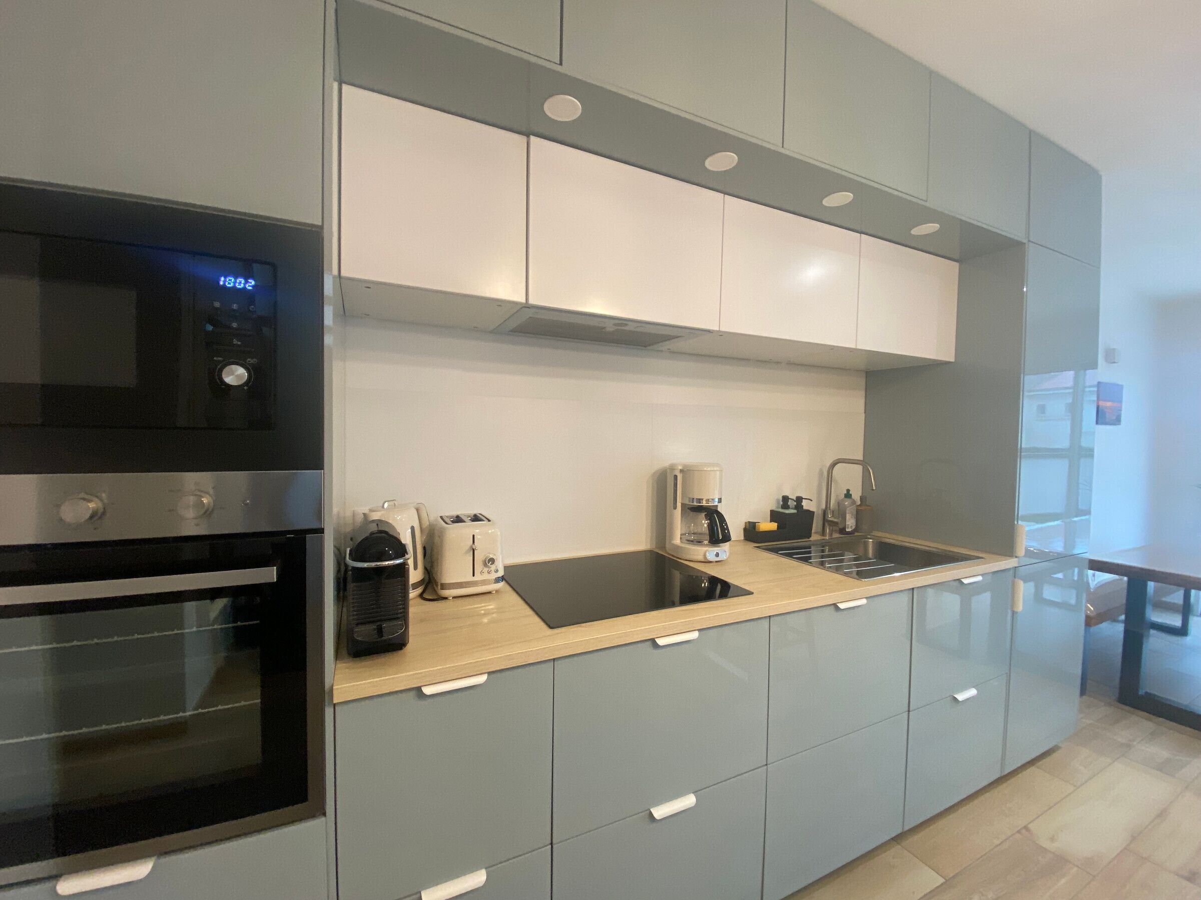 A modern kitchen with grey cabinets, a stainless steel oven, a microwave, a toaster, and a coffee maker.
