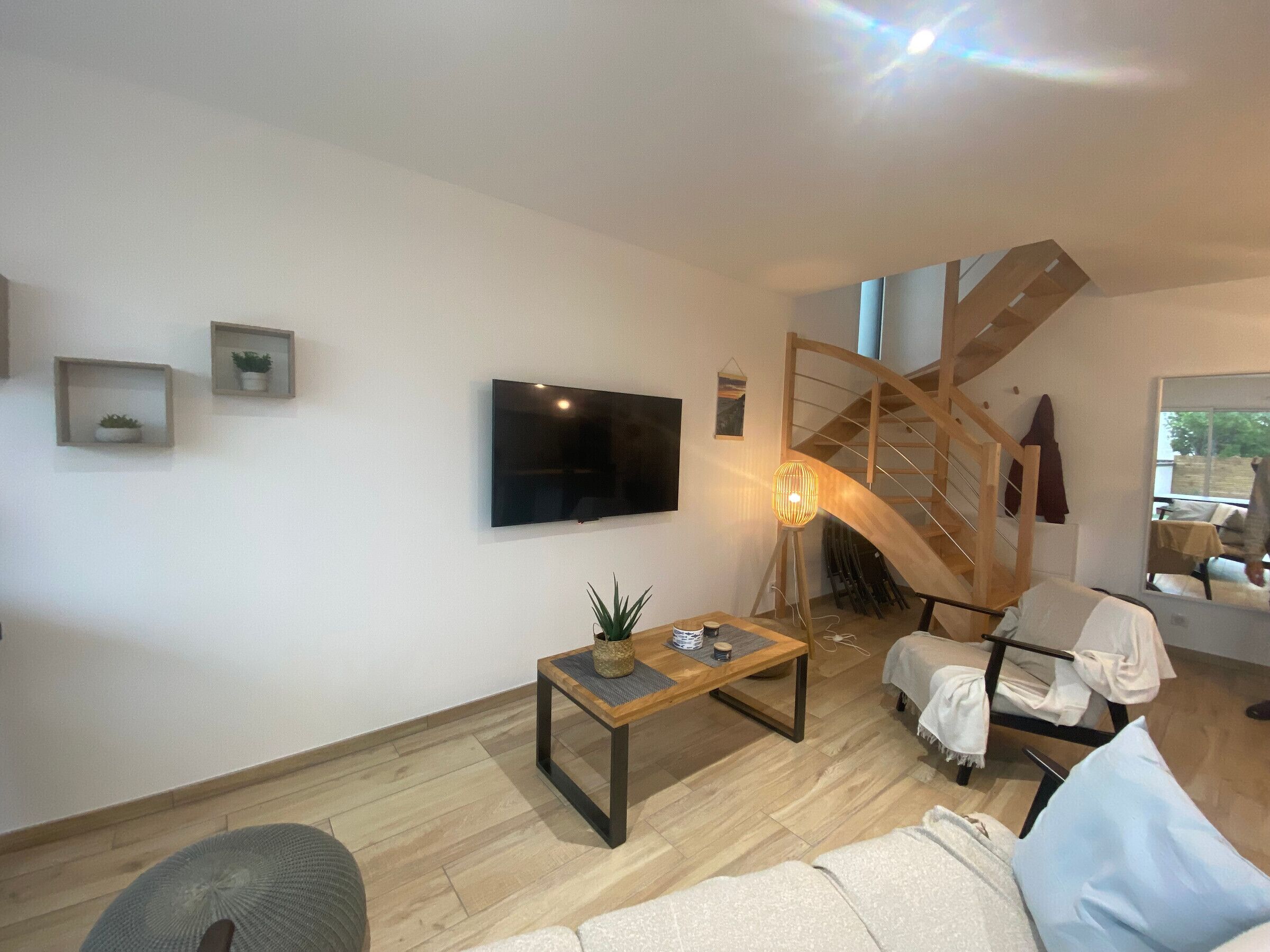 Una sala de estar moderna con televisor de pantalla plana, una mesa de centro de madera y una escalera.
