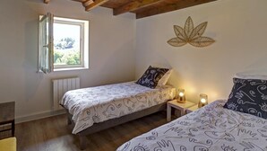 Une chambre avec deux lits, des poutres apparentes en bois au plafond, une fenêtre avec vue et un élément décoratif mural.