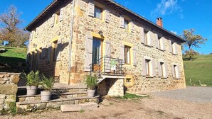Un bâtiment en pierre doté d’un balcon, d’un escalier menant à l’entrée et de plantes en pot.