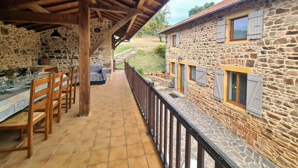 Un espace extérieur abrité, aménagé pour les repas, avec des murs en pierre, du mobilier en bois et un sol carrelé.