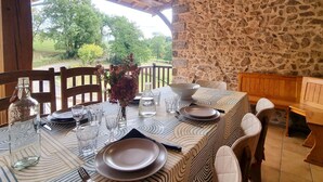 Une table dressée pour le repas, avec un mur en pierre en arrière-plan, des chaises en bois et un luminaire suspendu.