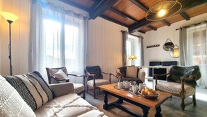Un salon chaleureux avec un plafond en bois, un canapé, des fauteuils, une table basse avec des tasses et des pâtisseries, et un téléviseur.