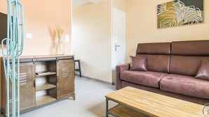 A living room with a brown sofa, a wooden coffee table, and a kitchenette with a cabinet and a hanging rack. - Cozy House with Sunny Terrace in Cuves (Cuves)