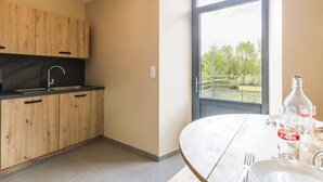 A modern kitchen with wooden cabinets, a black countertop, and a large window offering a view of greenery outside. - Cozy House with Sunny Terrace in Cuves (Cuves)