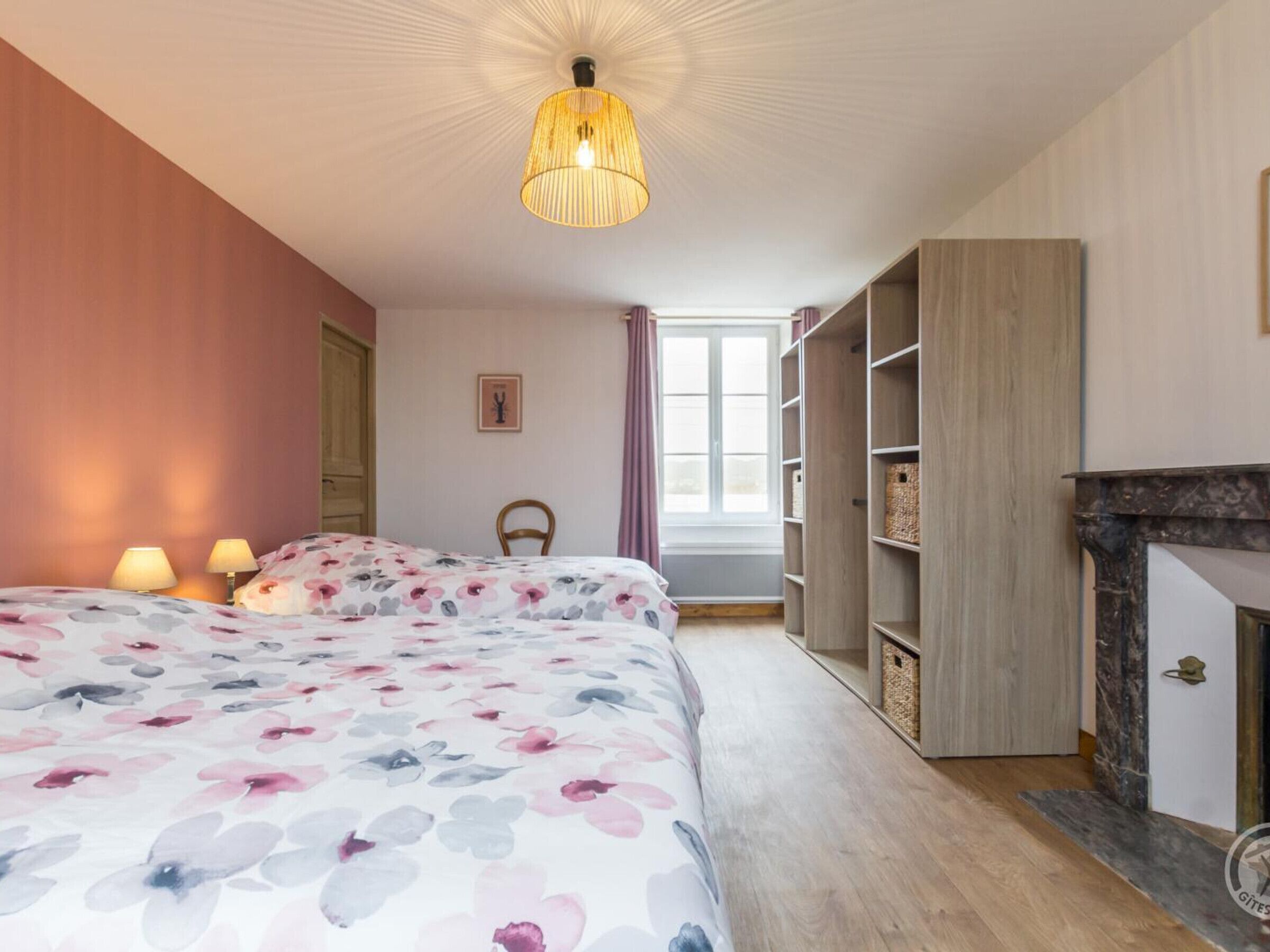 A bedroom with a bed, a hanging light fixture, a fireplace, and built-in shelving.