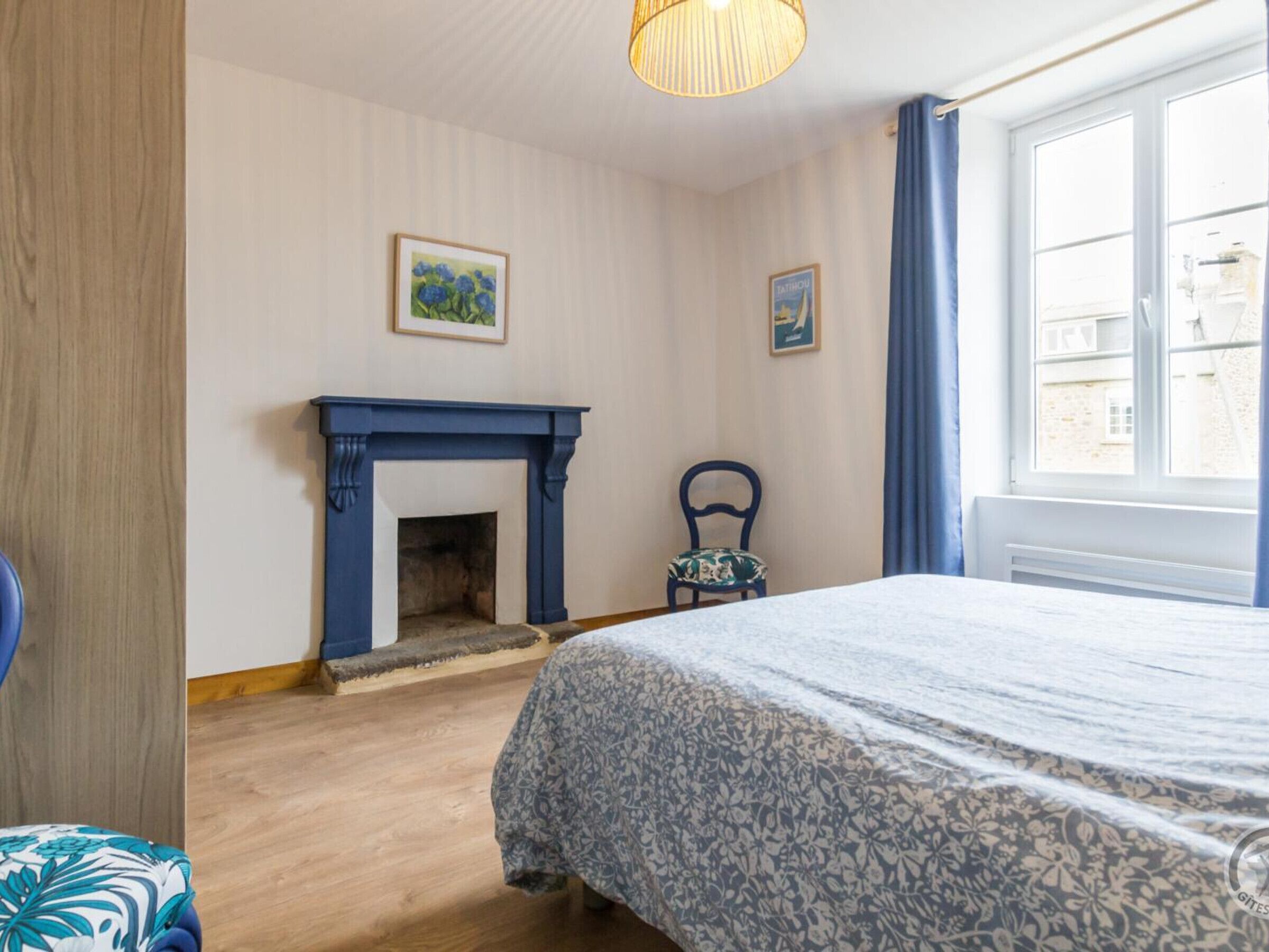 A bedroom with a bed, a blue fireplace, and a window with curtains.