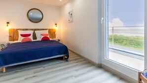 Une chambre à coucher avec un lit, un miroir rond et une fenêtre donnant sur un paysage verdoyant.