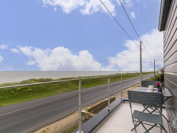 A balcony with a view of the sea, a table with chairs, and a railing.