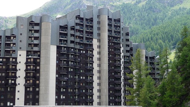 A high-rise building with multiple balconies, surrounded by a mountainous landscape.
