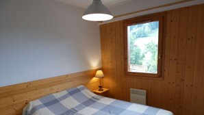 A bedroom with a bed, a window, a lamp, and wooden walls. - Beautiful 4-pers. apartment with balcony and garage in Grand-Bornand (Le Grand-Bornand)