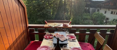 Ulkoterassi, jossa on puinen pöytä kahdelle ja pehmustetut tuolit pöydän ympärillä.