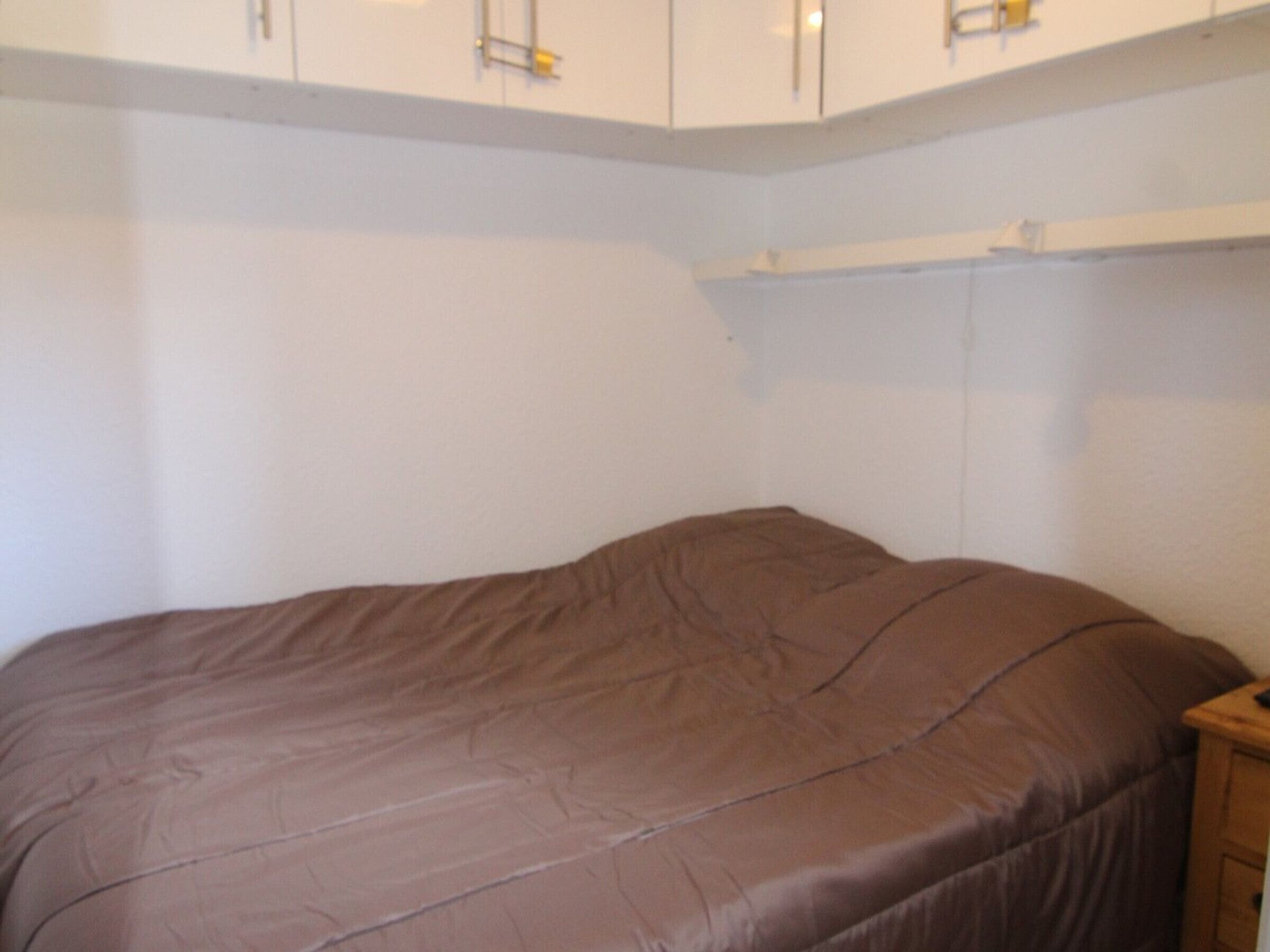 A bedroom with a single bed, a wooden nightstand, and white walls.
