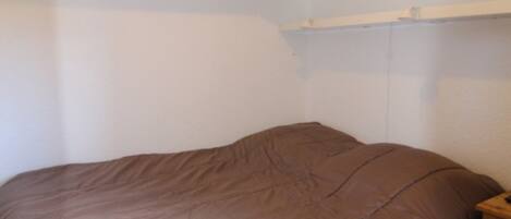 A bedroom with a single bed, a wooden nightstand, and white walls.