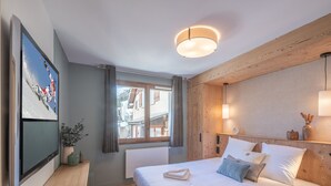 A modern hotel room with a large bed, a desk, a television, and a window with curtains. - Charming 3-room apartment with balcony and wifi in Huez (Huez)
