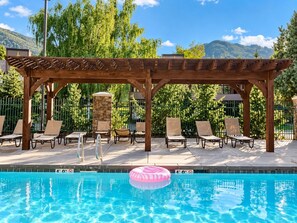 A pool area with a wooden pergola, lounge chairs, and a stone pillar. - Park City 4BR Condo | Private Hot Tub + Pool & Sauna | Walk or Shuttle to Park City Mountain (Park City)
