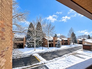 A snow-covered parking lot with a brick building and a row of trees in the background. - Park City 4BR Condo | Private Hot Tub + Pool & Sauna | Walk or Shuttle to Park City Mountain (Park City)