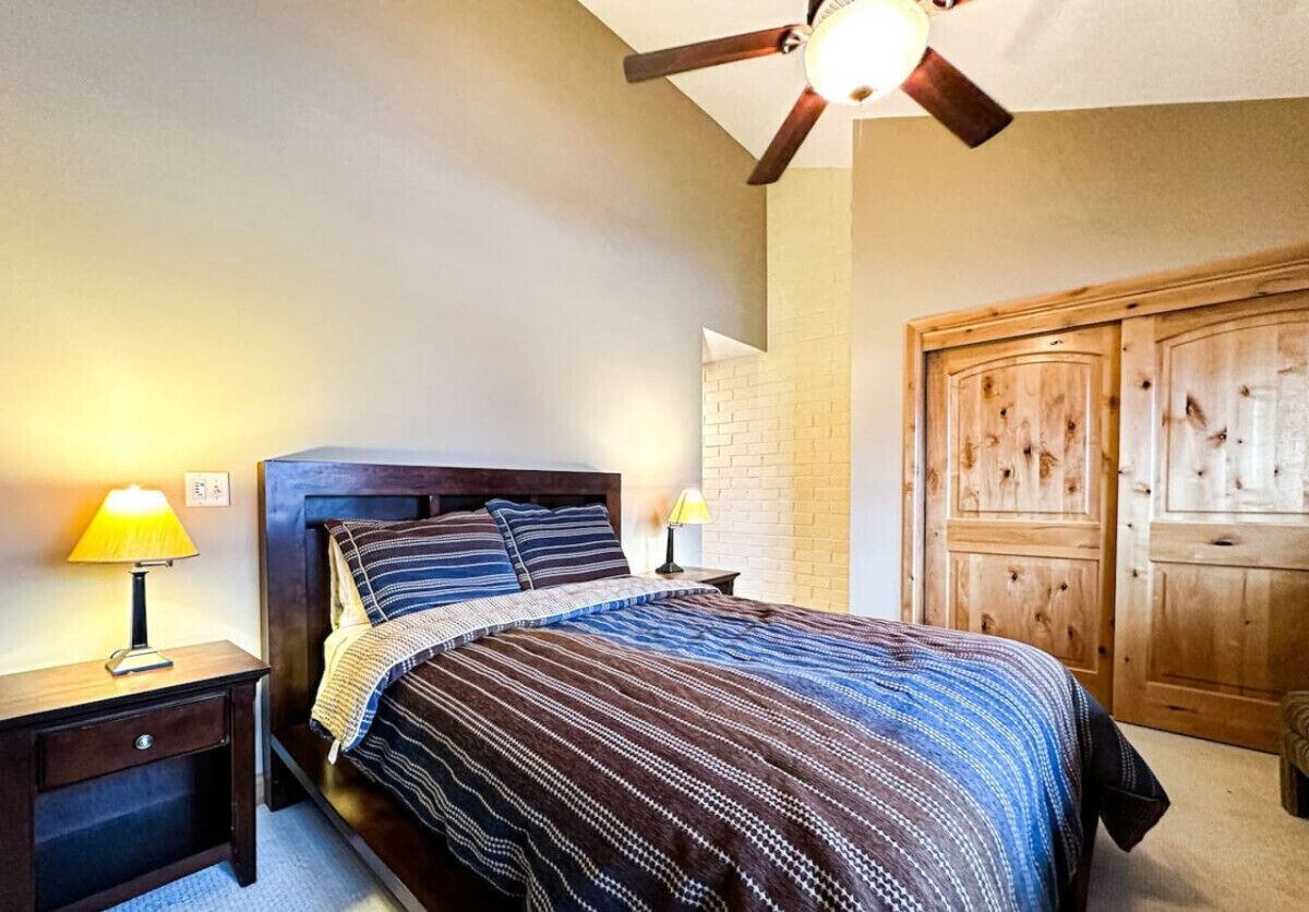 Ein Schlafzimmer mit einem Bett, zwei Nachttischlampen, einem Holzschrank und einem Deckenventilator.