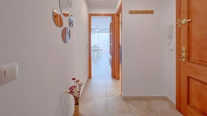 Un couloir avec une porte en bois, un téléphone fixé au mur et un vase rempli de fleurs.