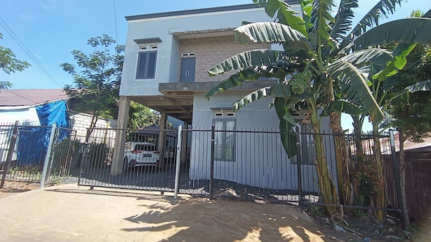 A two-story house with a balcony, surrounded by a metal fence, and a banana tree in the foreground. - Hotel O Pondok Tawing Rumbih (Tamban)