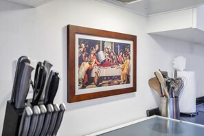 Une œuvre d’art encadrée représentant une scène historique avec des personnages autour d’une table, un porte-couteaux et un présentoir à ustensiles accrochés au mur.