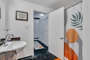 A bathroom with a white sink, a framed picture on the wall, and a shower curtain with leaf patterns.