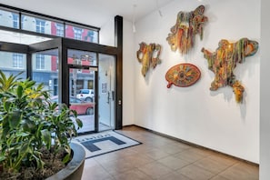 Un hall de hotel con puerta de vidrio, una planta en maceta y arte abstracto en la pared.