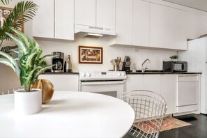 Une cuisine moderne avec des meubles blancs, une cuisinière, un four à micro-ondes et un coin repas comprenant une table et des chaises.