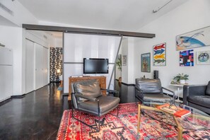 A modern living room with a flat-screen TV, leather chairs, a patterned rug, and artwork on the walls.