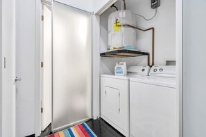 Un lavadero con calentador de agua, lavadora y dispensador de detergente.