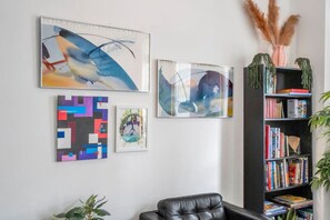 Una habitación con un sillón de cuero negro, una estantería con libros y tres obras de arte enmarcadas en la pared.