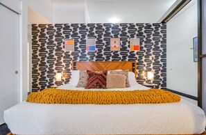 A bedroom with a patterned wall, a wooden headboard, and a yellow throw blanket.