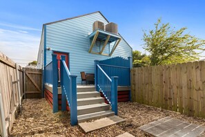 A small, single-story building with a blue exterior, a staircase leading to the entrance, and a wooden fence surrounding the property.