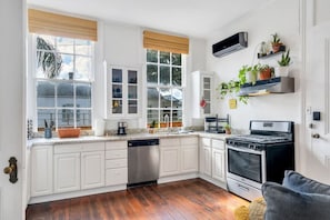 A kitchen with white cabinets, a dishwasher, a stove, and a window with a view of greenery.