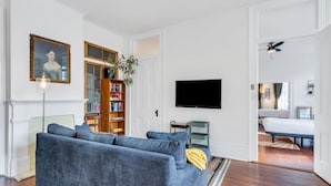 Ett vardagsrum med en soffa, en bokhylla, en tv och en dörr som leder till ett sovrum.