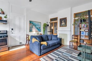 A living room with a blue sofa, wooden flooring, a painting on the wall, a bookshelf, and a fireplace.